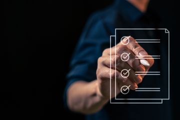 Person holding a pen interacting with a virtual checklist on a transparent screen.