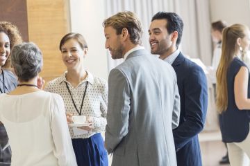 A diverse group of professionals networking and chatting at a business event in a bright, modern conference space.